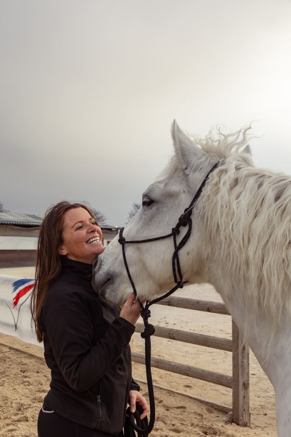 Elsa sourit près de son cheval blanc, une main sous son menton